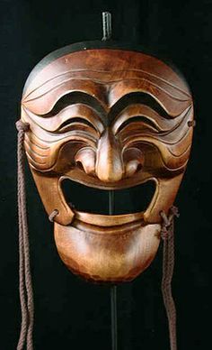 a wooden mask with a large smile on it's face and two strings hanging from the side