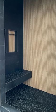 a black tiled shower stall with wooden walls and steps leading up to the toilet area