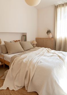 a bed sitting in a bedroom next to a window covered in white sheets and pillows