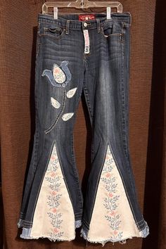 two jeans with embroidered flowers on them hanging from a clothes hanger in front of a brown background