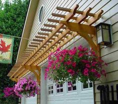 a wooden pergolan with flowers hanging from it's sides next to a garage