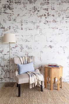 a chair and table in front of a white brick wall with a blue pillow on it