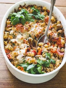 a white bowl filled with pasta, meat and veggies on top of a wooden table