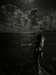 a woman standing in the ocean at night with clouds above her and full moon behind her