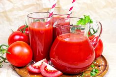 two pitchers of tomato juice and one pitcher with straws on a wooden platter