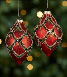 two red ornaments hanging from a christmas tree with lights in the backgroung