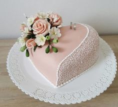 a heart shaped cake with pink frosting and white flowers on the top is sitting on a doily