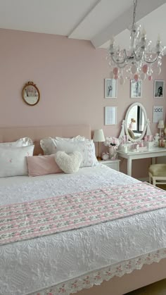 a bedroom with pink walls, white bedding and a chandelier hanging from the ceiling