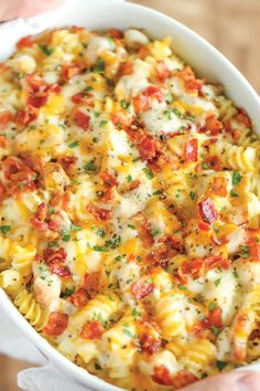 a white dish filled with macaroni and cheese covered in tomatoes, parsley