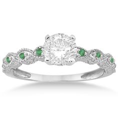 a white gold ring with green stones on the sides and an oval cut diamond in the center