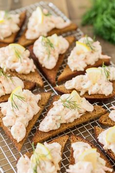 several pieces of bread topped with crab salad on top of a cooling rack and garnished with lemon wedges