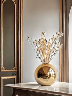 a gold vase filled with flowers sitting on top of a marble topped table next to a mirror