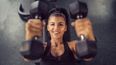 a woman lifting two dumbs in a gym