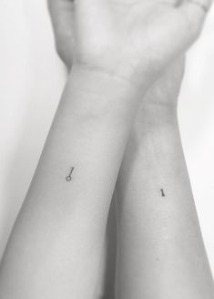 two hands holding each other with small tattoos on their wrist and one has an arrow in the middle