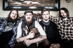 three men sitting on a couch holding a cat