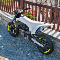 a white and yellow motorcycle parked on top of a cobblestone street next to a wooden fence