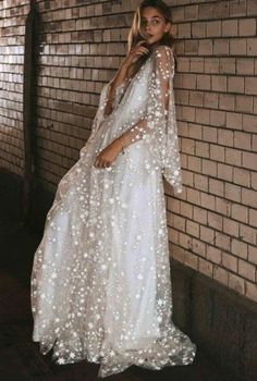 a woman standing in front of a brick wall wearing a white dress with stars on it