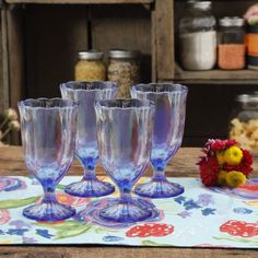 four wine glasses sitting on top of a table next to a vase with flowers in it