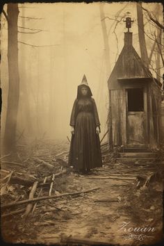 an old fashioned photo of a woman in a hooded costume standing next to a shack