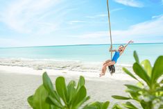 a woman swinging on a rope at the beach while holding onto a pole and smiling