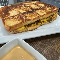 a grilled cheese sandwich on a white plate next to a bowl of mustard sauce