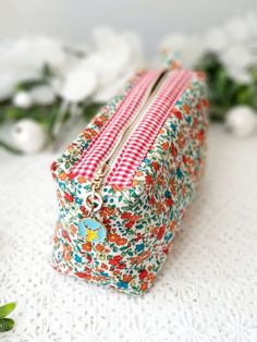 a small floral purse sitting on top of a white table next to flowers and greenery