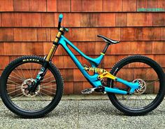 a blue and yellow mountain bike parked in front of a brown building with wooden siding