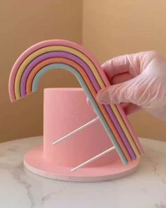 a person in pink gloves is holding up a rainbow shaped paper holder on top of a marble table