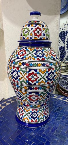 a large colorful vase sitting on top of a blue tiled table next to a white wall