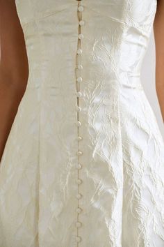 the back of a woman's white wedding dress with buttons and pearls on it