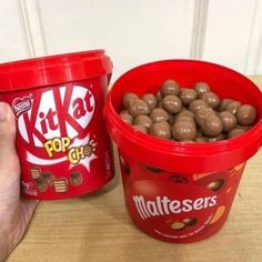 a hand holding a container of kitkats next to a bucket of chocolate candies