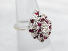 This sophisticated ring is crafted with lustrous white gold and adorned with shining white diamonds and sparkling red rubies. Each gem is carefully chosen and placed in a unified design, creating a stunning piece of jewelry to treasure for a lifetime.Metal: 14K White GoldGem: 11 Diamonds totaling .34 Carats, VS-SI in Clarity, H-I in ColorGem Measurements: 3.1 mm, RoundAccents: 16 Rubies totaling .64 CaratsRing Size: 5.75Marks: "14K-ODI" Stamped on the inside band Luxury Red Cluster Diamond Ring, Red Cluster Diamond Ring With Brilliant Cut, Cluster Ruby Diamond Ring With Center Stone, Formal Cluster Ruby Ring, Formal Ruby Ring With Diamond Accents In Cluster Shape, Luxury Silver Ruby Ring With Single Cut Diamonds, Ruby Ring With Diamond Cluster And Brilliant Cut, Cluster Ruby Ring With Brilliant Cut Diamonds, Cluster Ruby Ring With Rose Cut Diamonds