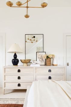 a white dresser with two lamps on top of it and pictures above the drawers in front of them