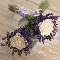 three white roses and lavenders in a vase on a wooden table with purple ribbons