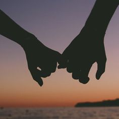 two people holding hands while standing in front of the ocean