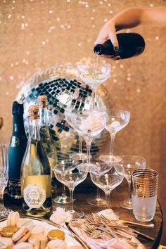 champagne being poured into wine glasses in front of disco ball and confetti plates