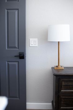 the lamp is on in front of the door and next to the dresser with it's drawer open