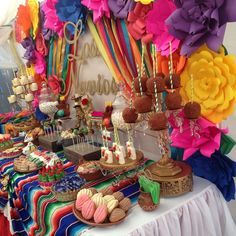 a table topped with lots of desserts next to a rainbow colored wall covered in paper flowers