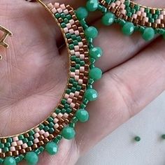 a pair of green and gold beaded hoop earrings on someone's left hand