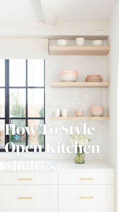 an open kitchen shelving with white cabinets and wooden shelves in front of a window