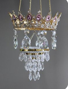 a gold crown hanging from the ceiling with pink and purple crystals on it's sides