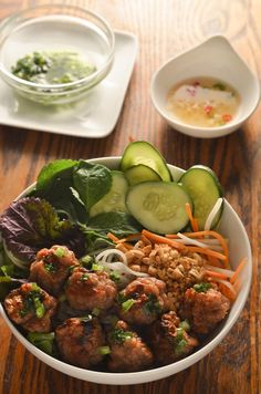 a bowl filled with meatballs and vegetables next to some dipping sauce on the side