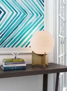 a lamp sitting on top of a wooden table next to some books and a painting