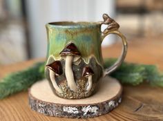 a ceramic mug with mushrooms on it sitting on top of a wooden table next to pine needles