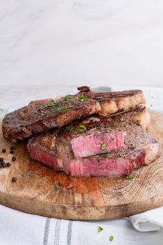 two pieces of steak sitting on top of a wooden cutting board