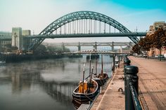 two boats are tied up on the side of the water near a bridge and buildings