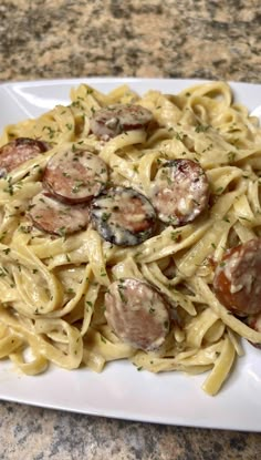 a white plate topped with pasta covered in sausage and sauce on top of a marble counter