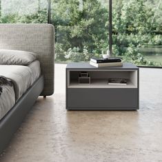 a bed sitting next to a nightstand with books on top of it in front of a window