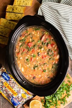 a black crock pot filled with soup next to sliced bread