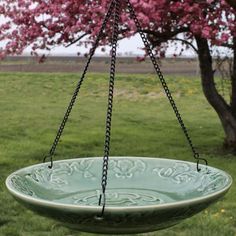 a green bowl hanging from a chain in front of a tree with pink flowers on it